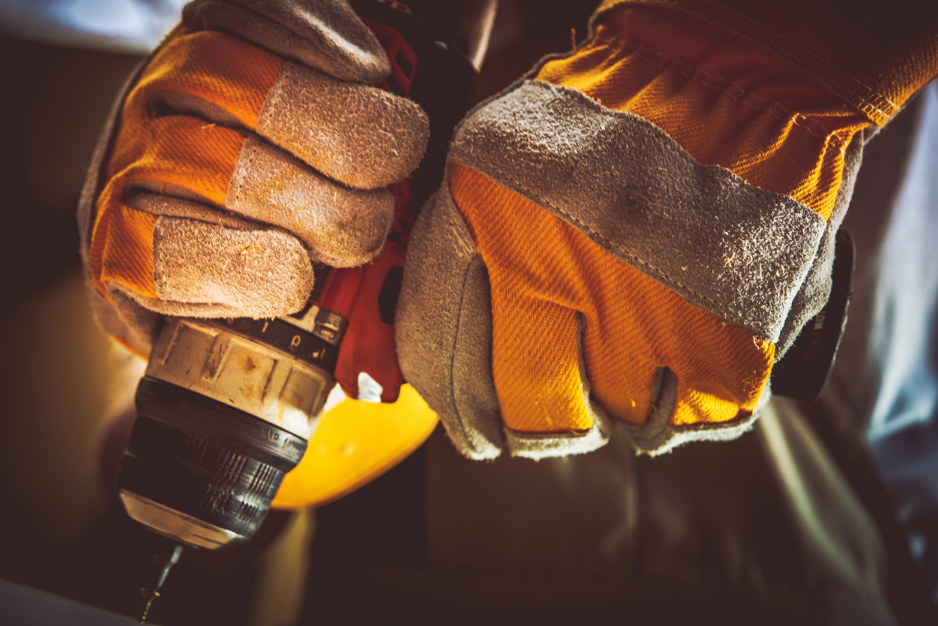 Close-up of a Cherry Hill handyman in heavy-duty work gloves gripping a cordless power drill on a job site